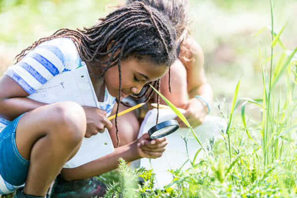 two younbg students with magnifying glasses inspecting the grass